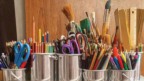 Art supplies ranging from scissors to colored pencils in varius cans.