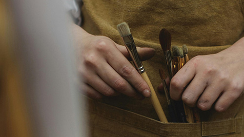 A person adjusting paintbrushes in their apron.