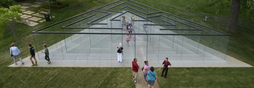Guests explore inside and around the triangular glass labyrinth structure in the museum's Sculpture Park.