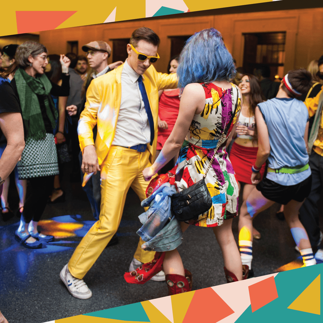 A man in a yellow suit and a woman in an colorfully patterned dress dance in a crowd at a Nelson-Atkins event similar to Night/Shift.